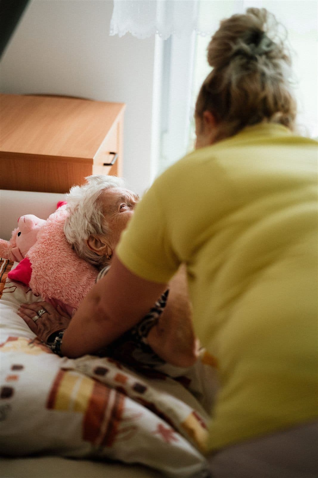 Une intervenante aide avec douceur une personne âgée à se redresser dans son lit