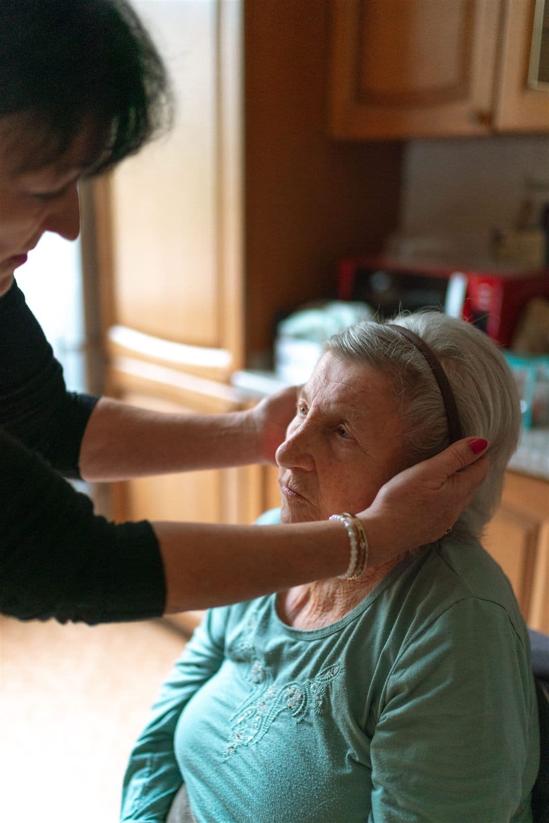 Une intervenante ajuste avec douceur la coiffure d'une dame âgée